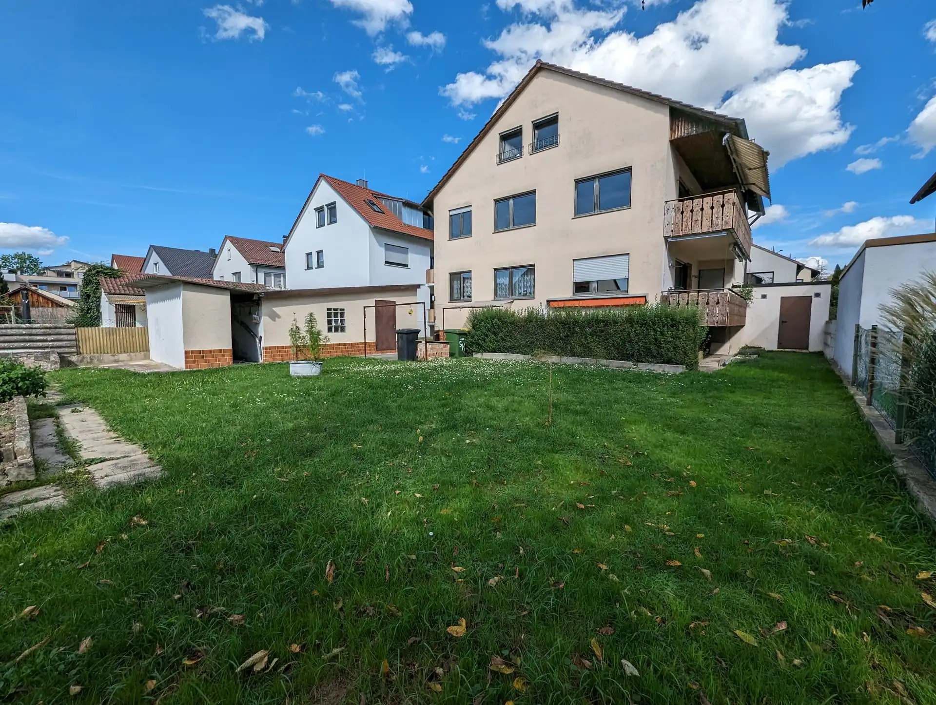 Mehrfamilienhaus mit großem Garten, einer Garage und mehreren dinklen Balkonen.