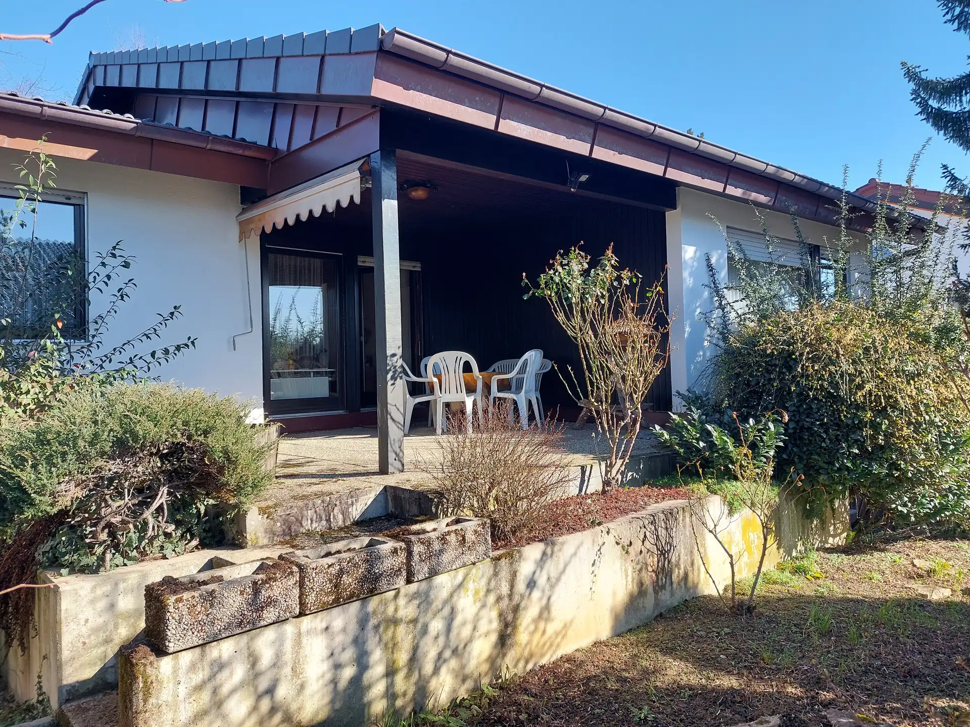 Bungalow mit überdachter Terrasse und kleiner erhöhter Steinmauer vor der Terrasse