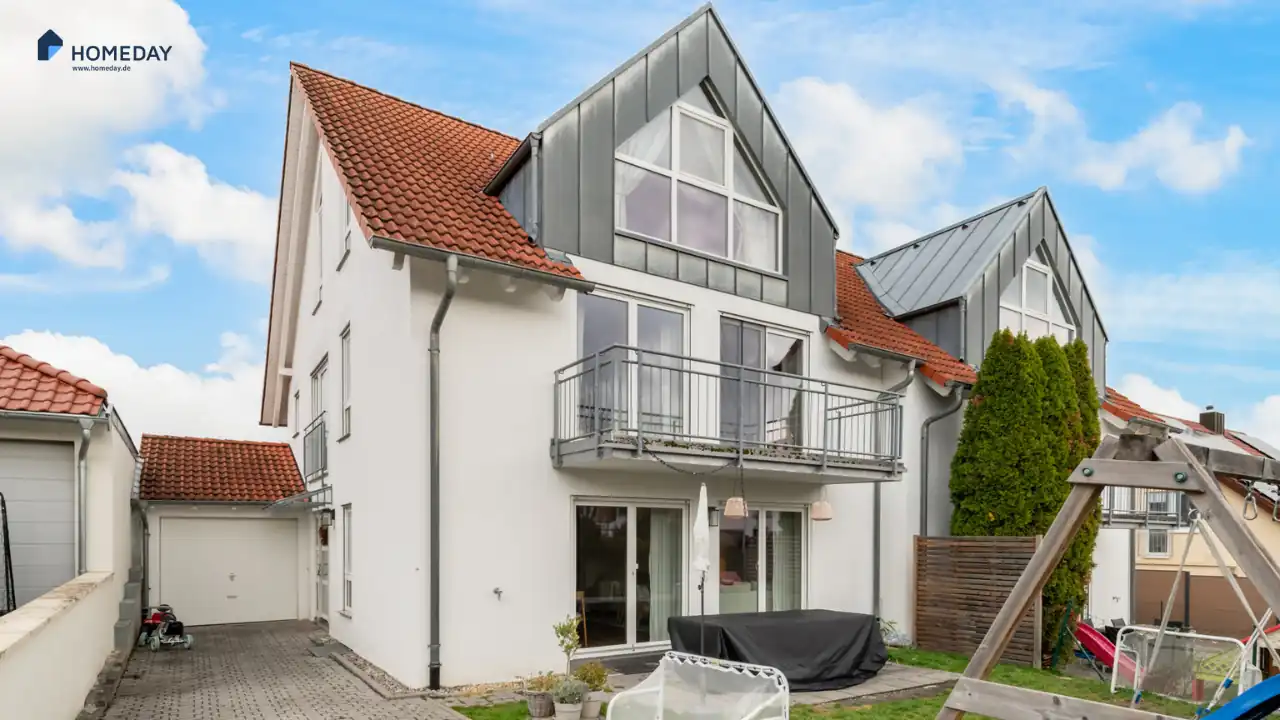 Weißes Mehrfamilienhaus mit rotem Dach und großer Gaupe im Dachgechoss neben einer Tiefgarageneinfahrt